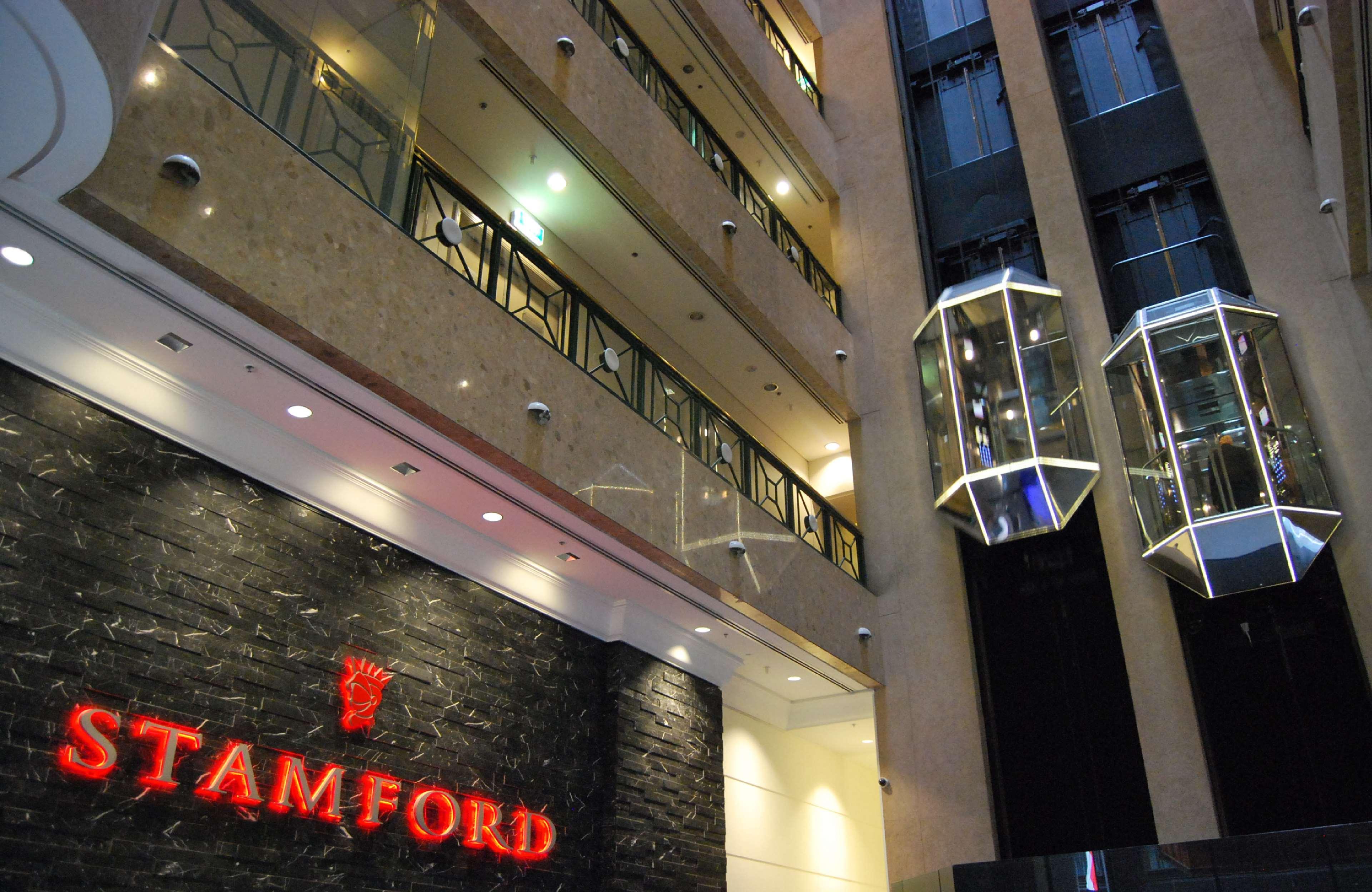 墨尔本斯坦福广场酒店 外观 照片 The photo shows the interior of a building, likely a hotel or commercial space. There is a prominent sign with the name "STAMFORD" in red lettering against a dark stone background. The building features several floors, visible from the photograph, wi