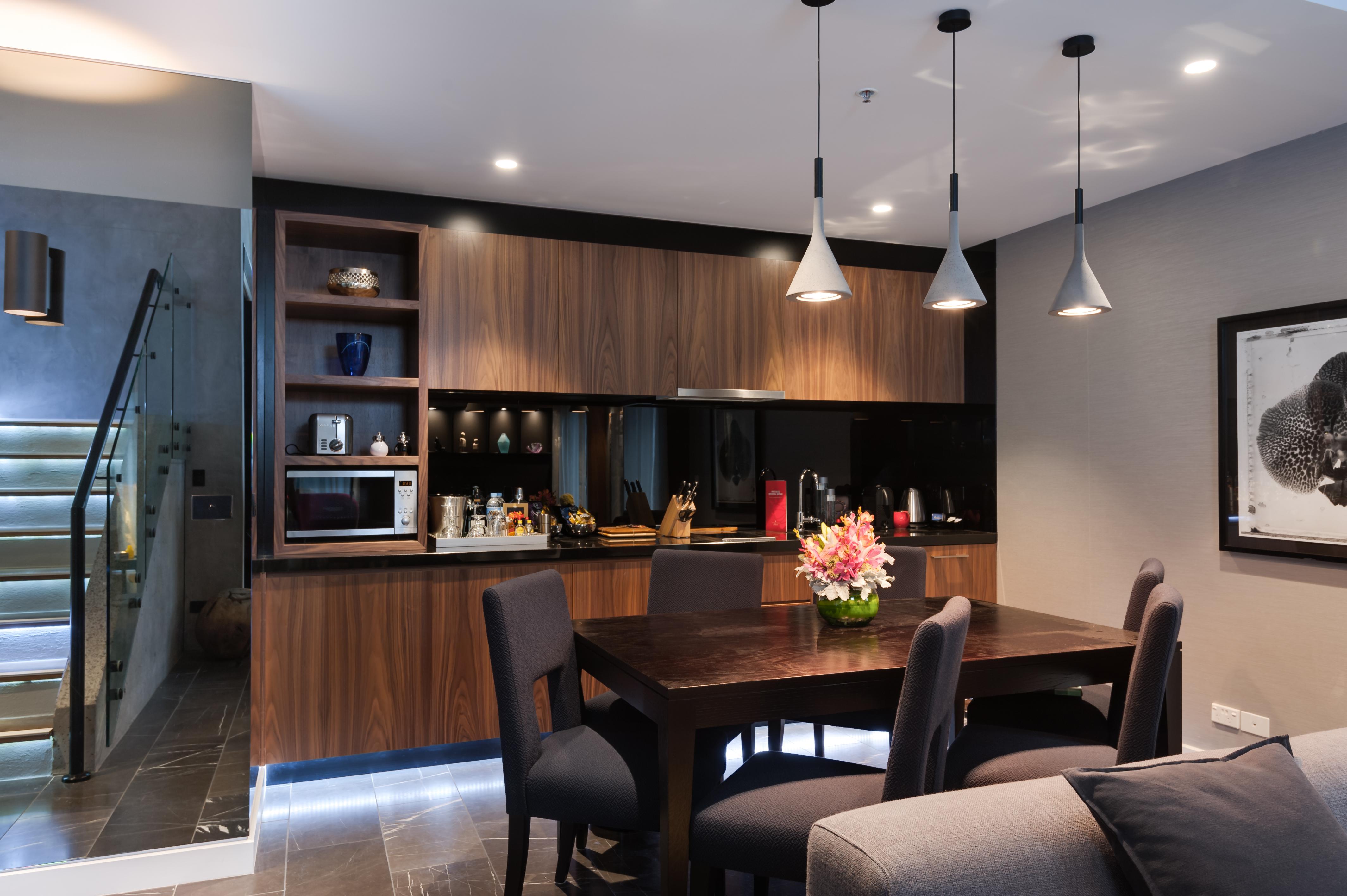 墨尔本斯坦福广场酒店 外观 照片 The image shows a modern kitchen and dining area. The kitchen features dark wooden cabinetry with black accents, a microwave, and various kitchen items arranged on the shelves. There is a dining table made of dark wood, surrounded by several chairs. 