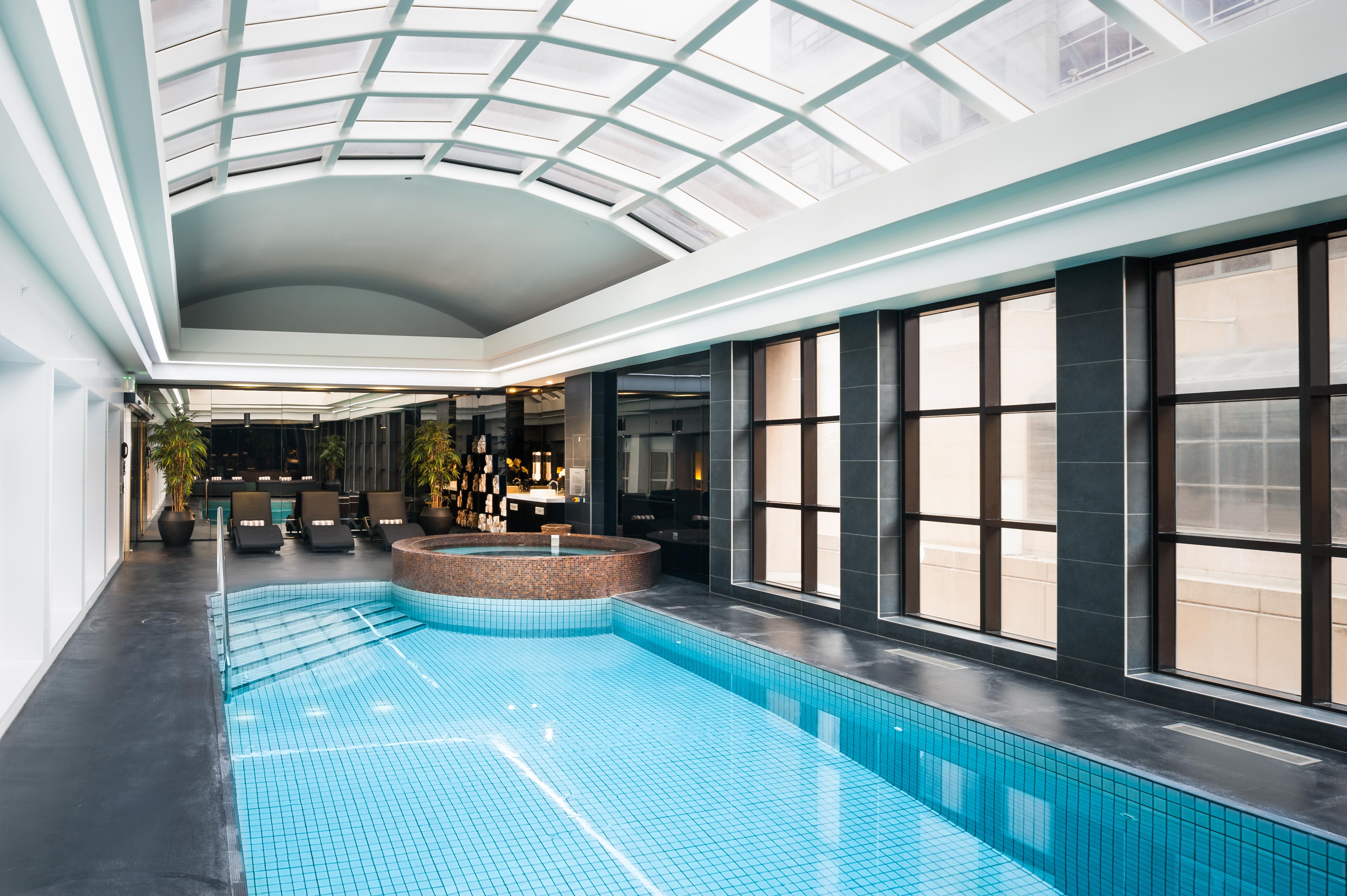 墨尔本斯坦福广场酒店 外观 照片 The photo shows an indoor swimming pool area with a modern and sleek design. The pool is rectangular and features bright blue tiles. Above the pool, there's a large, transparent glass ceiling that allows natural light to flood the space. Surrounding 