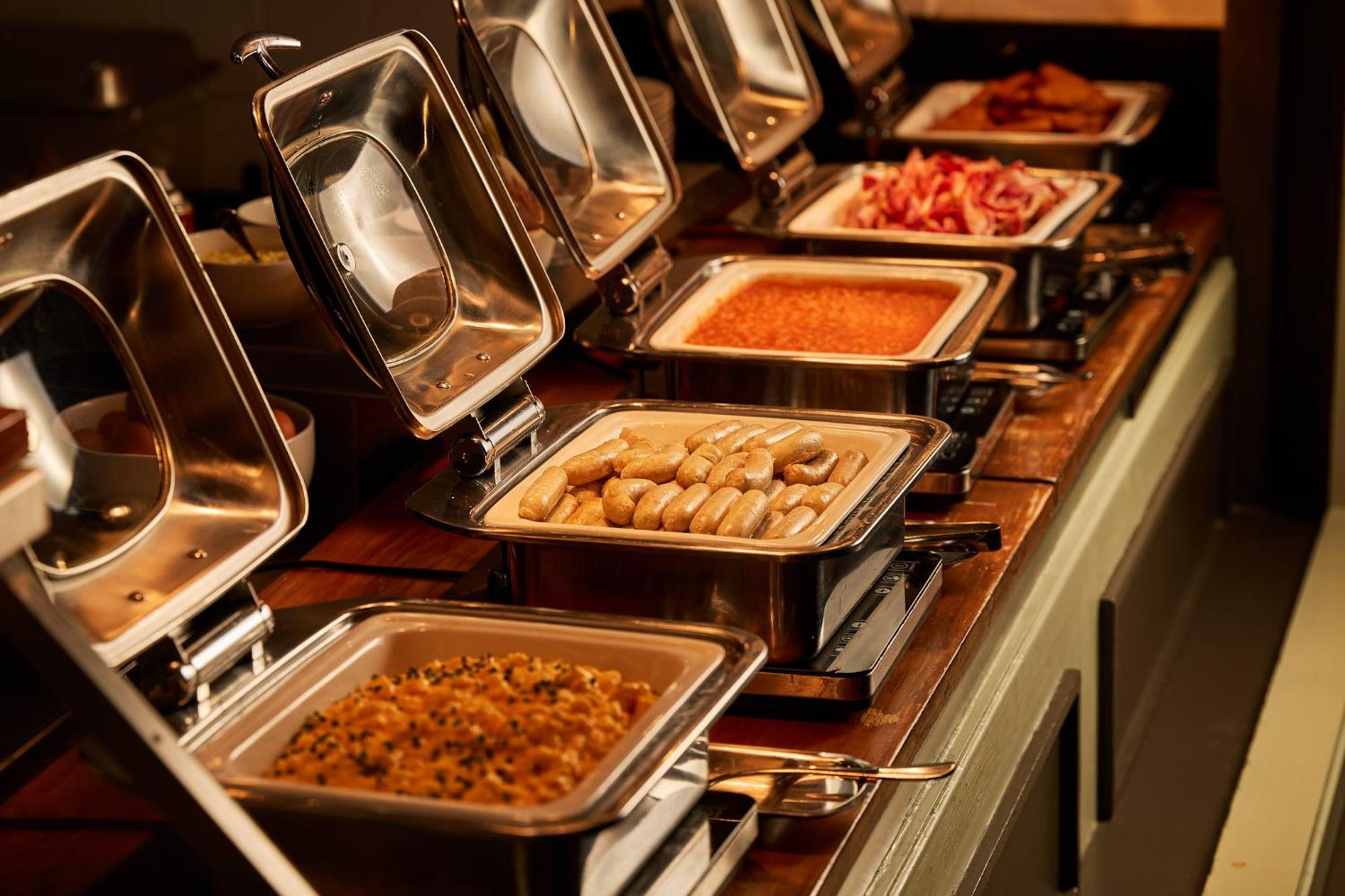 墨尔本斯坦福广场酒店 外观 照片 The photo depicts a buffet setup featuring multiple food trays in stainless steel chafing dishes. Each dish is opened to display different types of food. The dishes contain a variety of items, which might include a mix of proteins, vegetables, or sta
