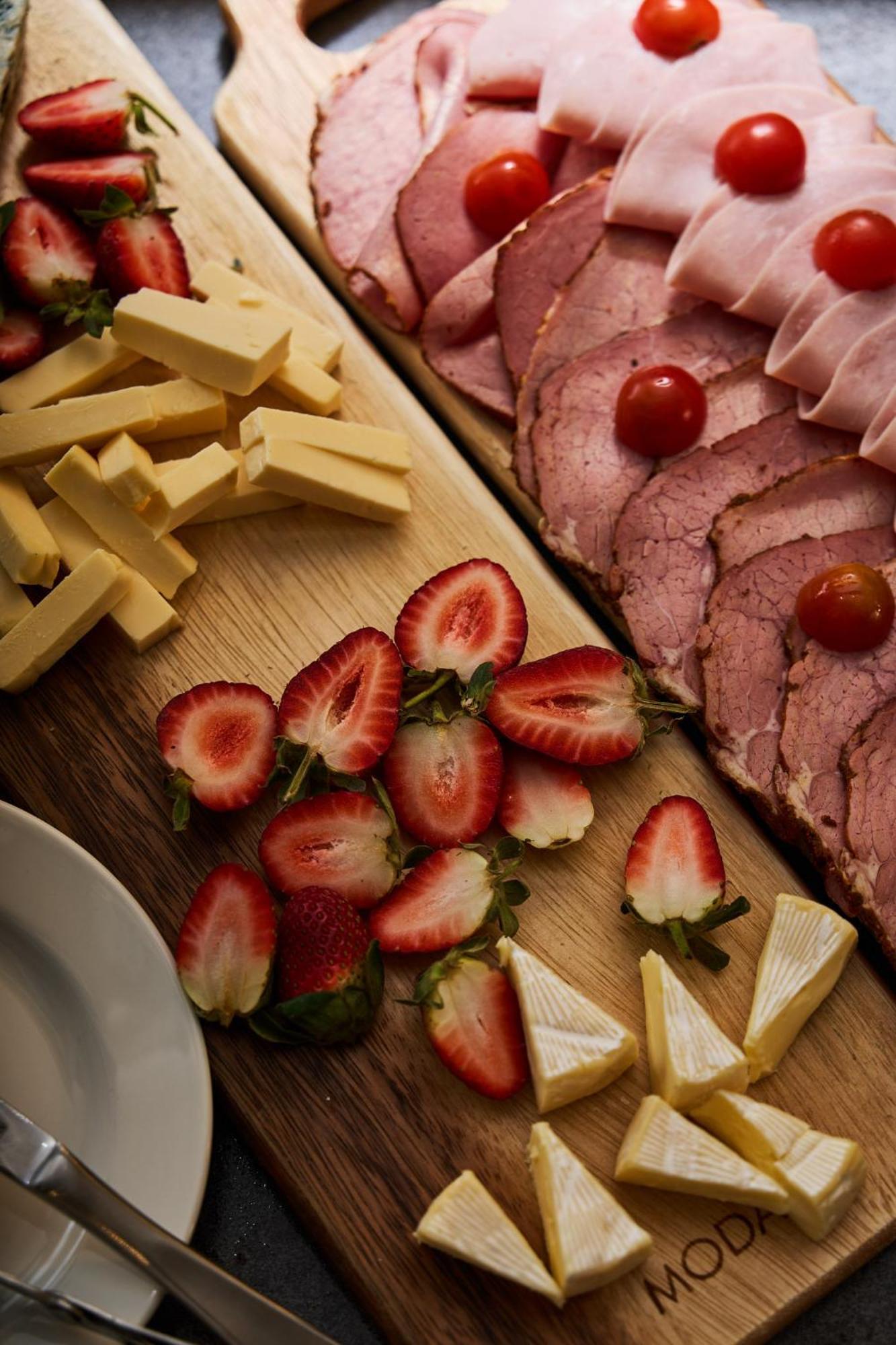 墨尔本斯坦福广场酒店 外观 照片 The photo displays an assortment of food items arranged on a wooden surface. There are slices of various meats, including ham, alongside round cherry tomatoes. Next to the meat, there are several pieces of yellow cheese cut into sticks. Additionally,