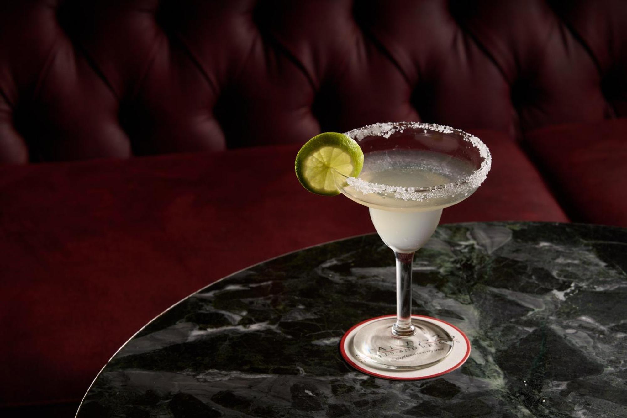 墨尔本斯坦福广场酒店 外观 照片 The photo shows a beautifully presented margarita cocktail served in a classic margarita glass. The drink is clear with a salt rim around the edge, and adorned with a slice of lime. The glass is placed on a dark green marble table, contrasting with a