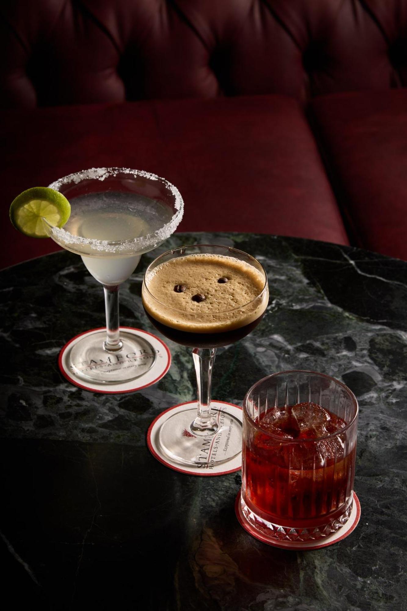 墨尔本斯坦福广场酒店 外观 照片 The photo displays three different cocktails arranged on a dark marble table. 

1. On the left, there is a margarita glass filled with a clear drink, garnished with a lime slice and featuring a salted rim.
2. In the center, a coupe glass holds a dark
