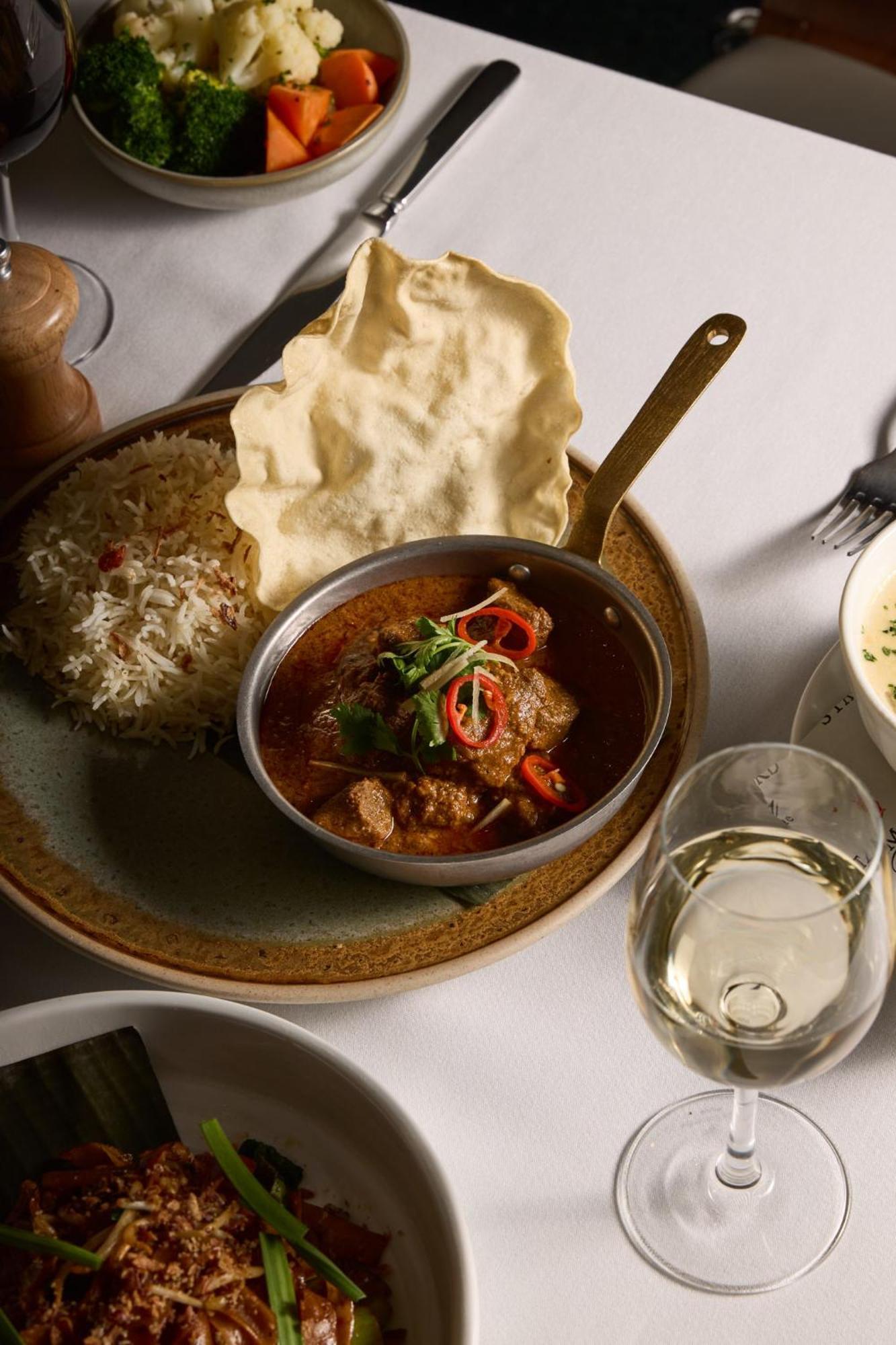 墨尔本斯坦福广场酒店 外观 照片 The photo features a plated meal that includes a serving of meat curry in a small round dish. The curry is garnished with herbs and slices of chili. Accompanying the curry, there is a mound of fluffy rice, and a piece of crispy flatbread (poppadom) r