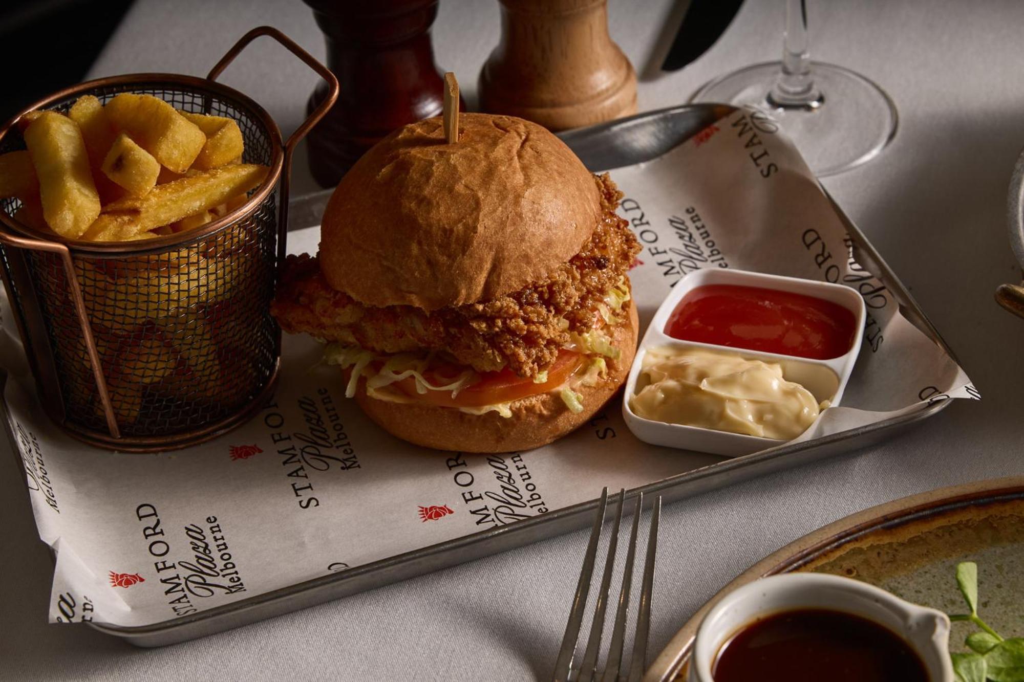 墨尔本斯坦福广场酒店 外观 照片 The photo features a meal served on a tray. In the center is a sandwich made with a golden-brown chicken fillet that appears crispy, placed inside a soft bun. The sandwich is likely complemented by some type of sauce or condiments underneath the chic