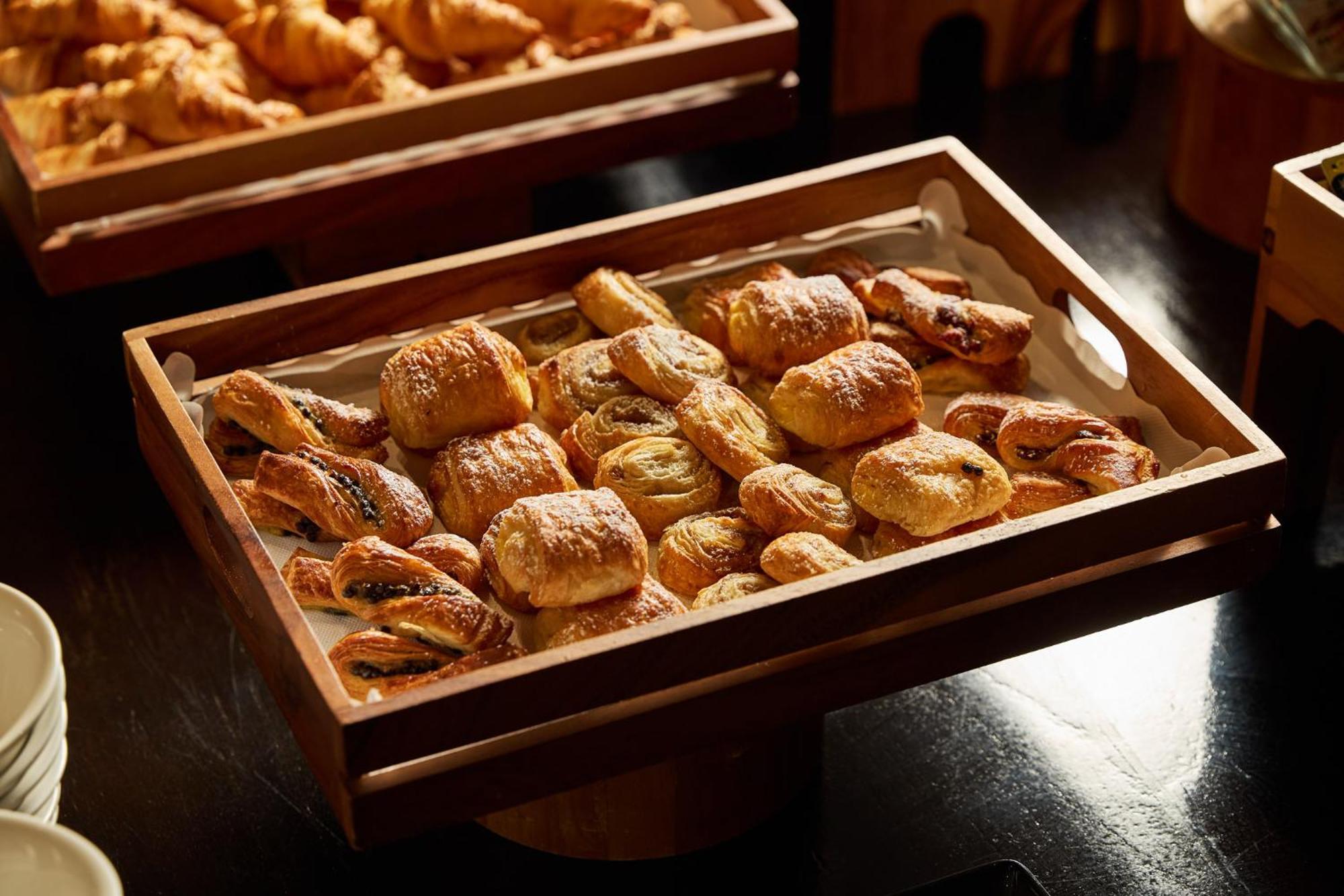 墨尔本斯坦福广场酒店 外观 照片 The photo shows a wooden tray filled with an assortment of baked goods. There are various types of pastries, including small, flaky items that appear to be puff pastries, and possibly some filled with chocolate or fruit. The pastries are golden brown