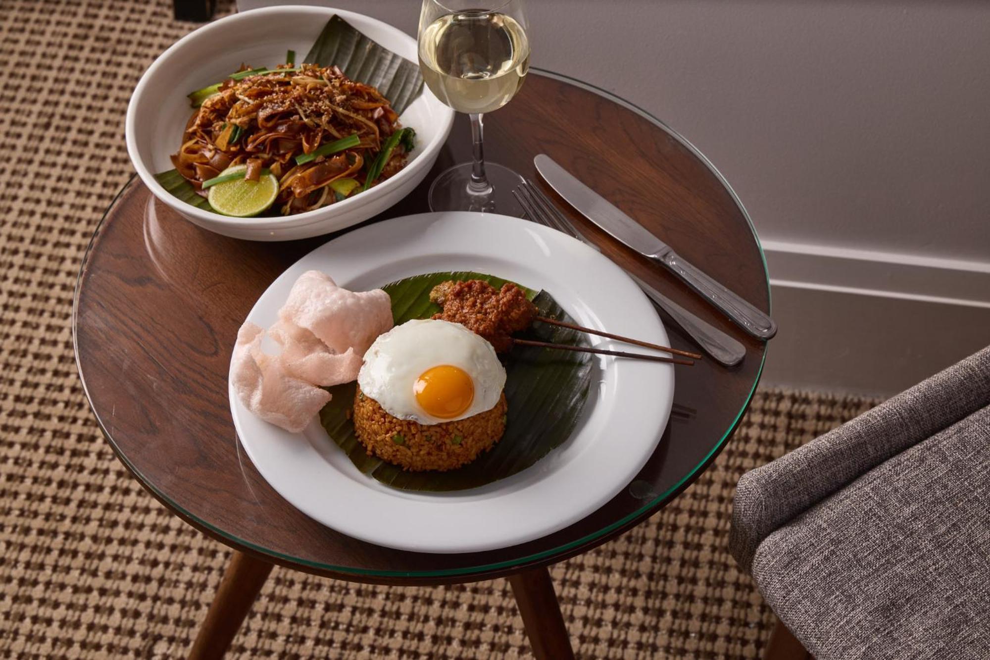 墨尔本斯坦福广场酒店 外观 照片 The photo shows a beautifully arranged meal on a wooden side table. On a white plate, there is a serving of fried rice, topped with a sunny-side-up egg, accompanied by prawn crackers. The dish also features a small portion of what appears to be a spi